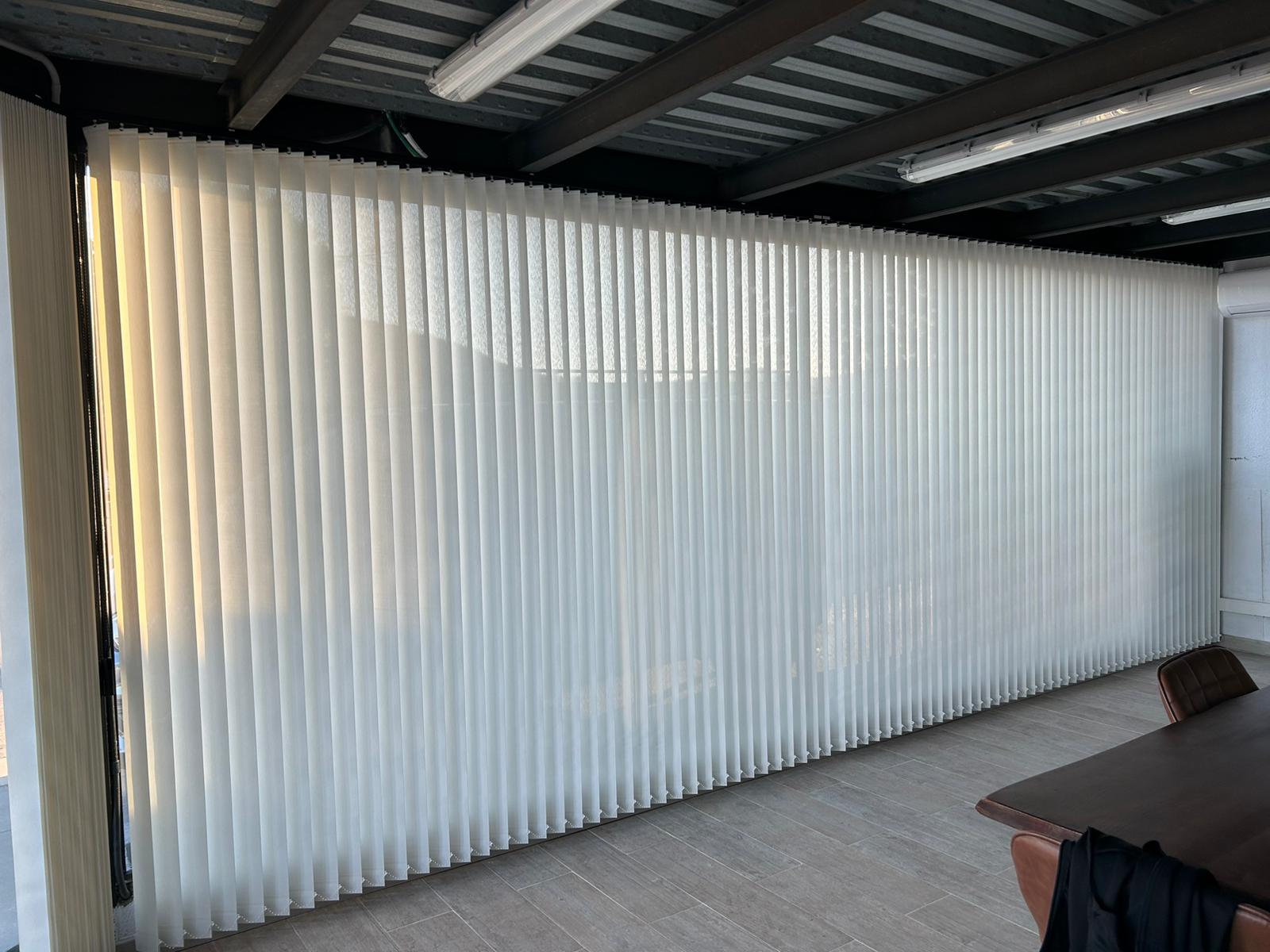 Cortina de lamas verticales de 89mm de color blanco instalada en cristalera grande de oficina