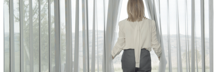 Cortina Allusion instalada en ventanal grande, mientras una persona pasa entre la cortina sin necesidad de accionarla